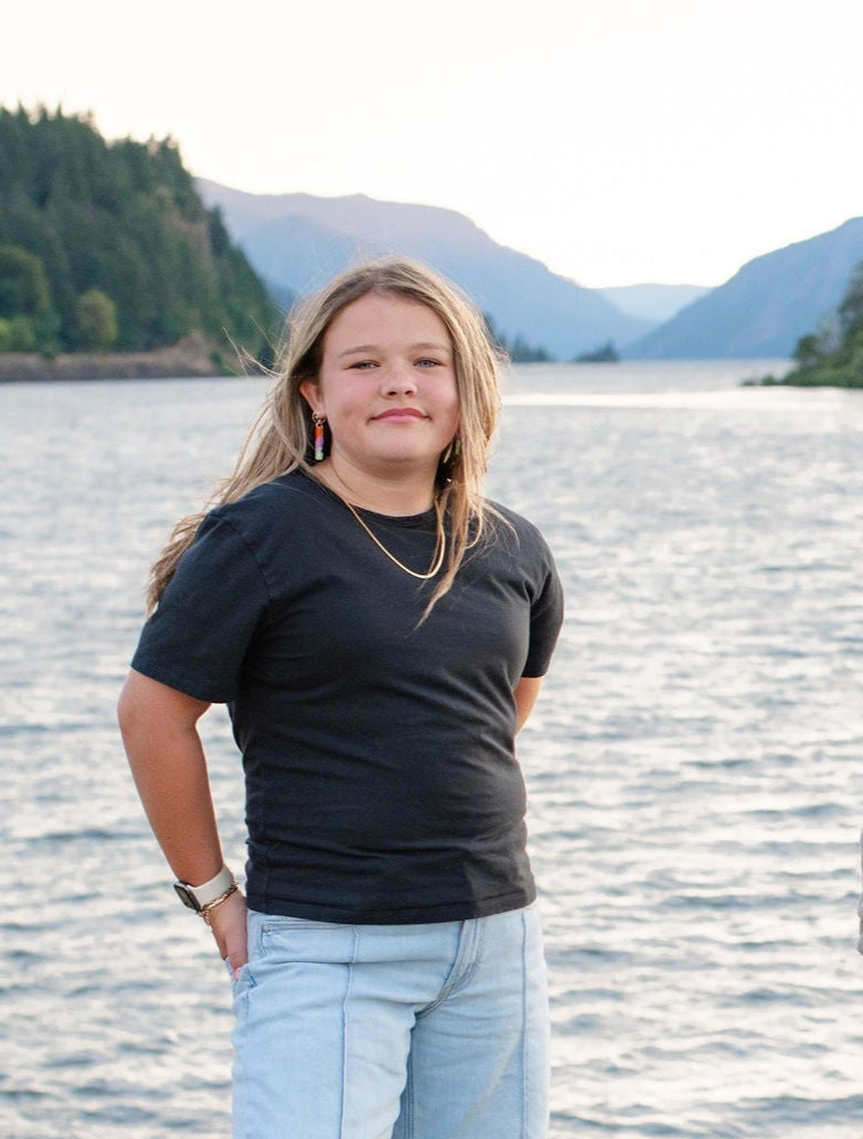 Girl standing by a river with mountains in the background